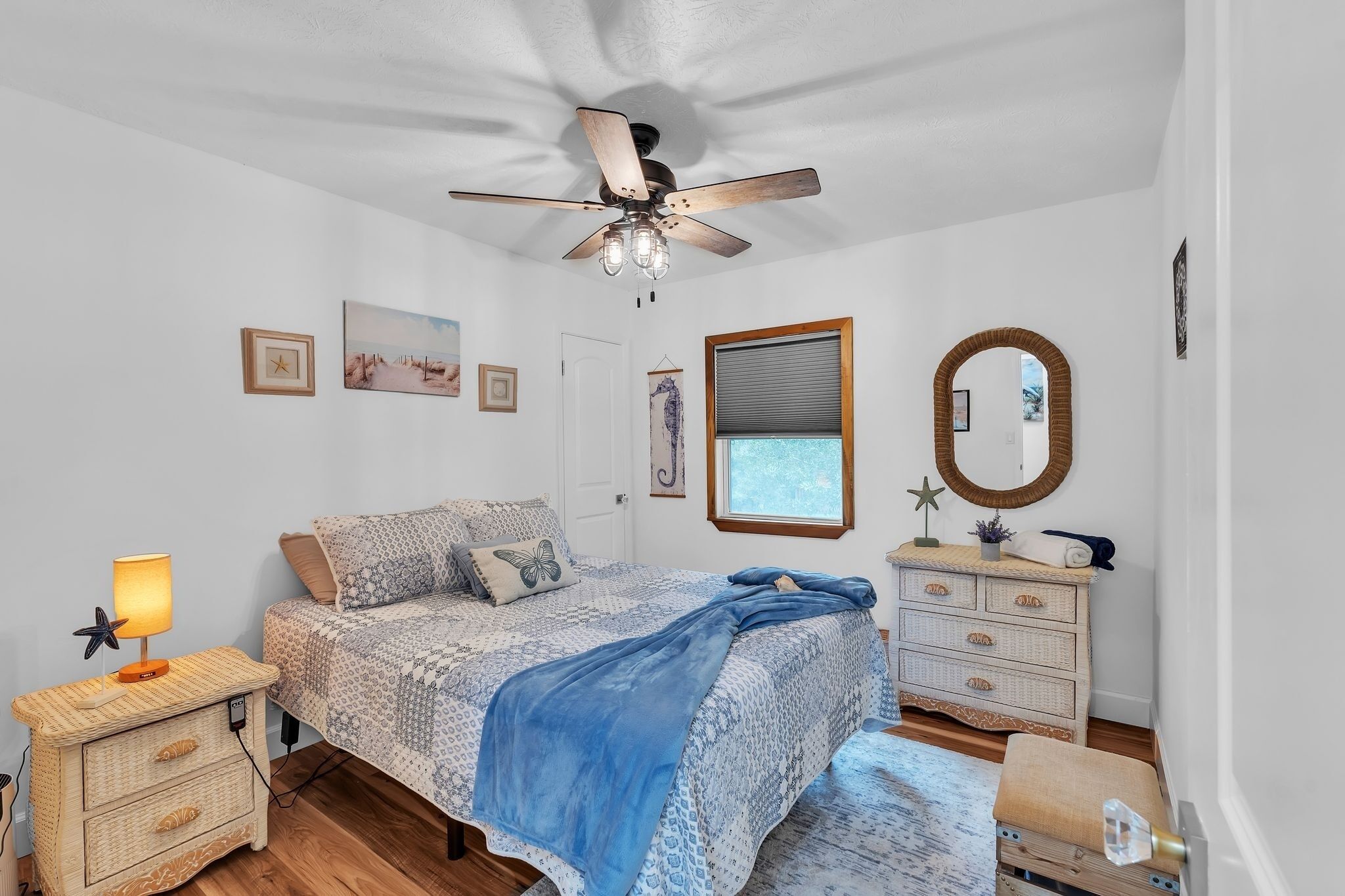 A bedroom with a bed, a ceiling fan, a bedside lamp, a dresser, a mirror, and a window with blinds.