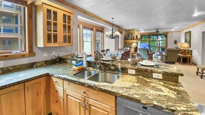 A kitchen with granite countertops, wooden cabinets, a dishwasher, and a dining area with a table and chairs.