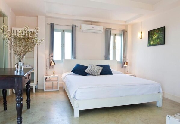 A bedroom with a white bed, two pillows, a bedside table, a lamp, an air conditioning unit, and a vase with flowers. - Villa Duang Champa (Chiang Mai)