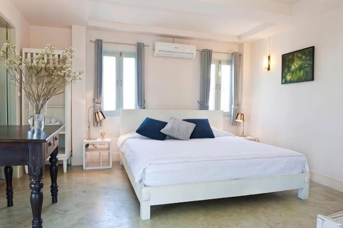 A bedroom with a white bed, bedside tables, a desk, and a vase with flowers.