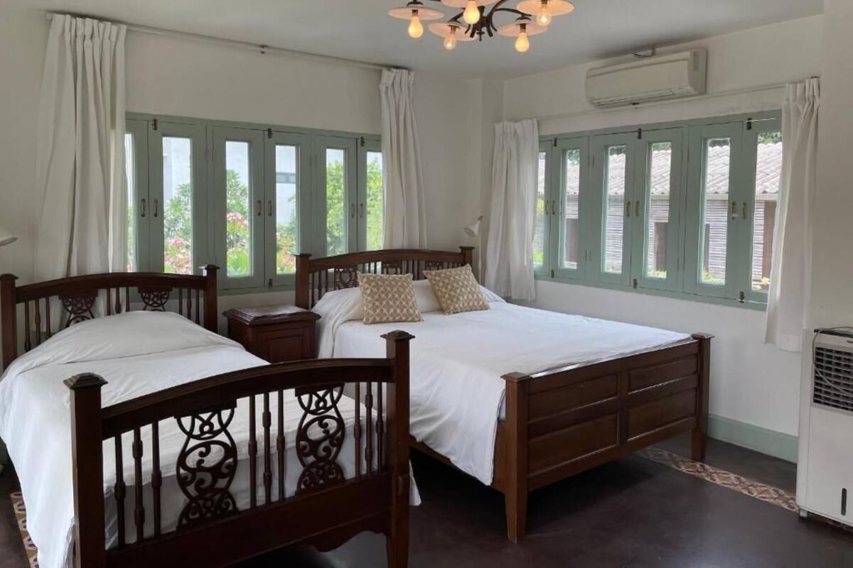 Een slaapkamer met twee houten bedden, een kroonluchter en een raam met gordijnen.