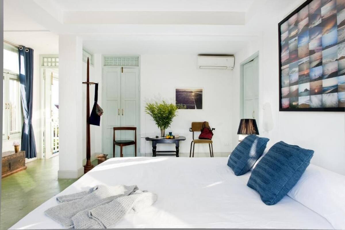 Een slaapkamer met een groot bed, een klein tafeltje met een plant, een stoel en een luchtverfrisser aan de muur.