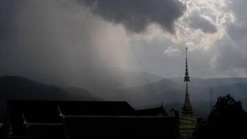 Um edifício tradicional com telhado pontiagudo e torre, com montanhas e céu nublado ao fundo.