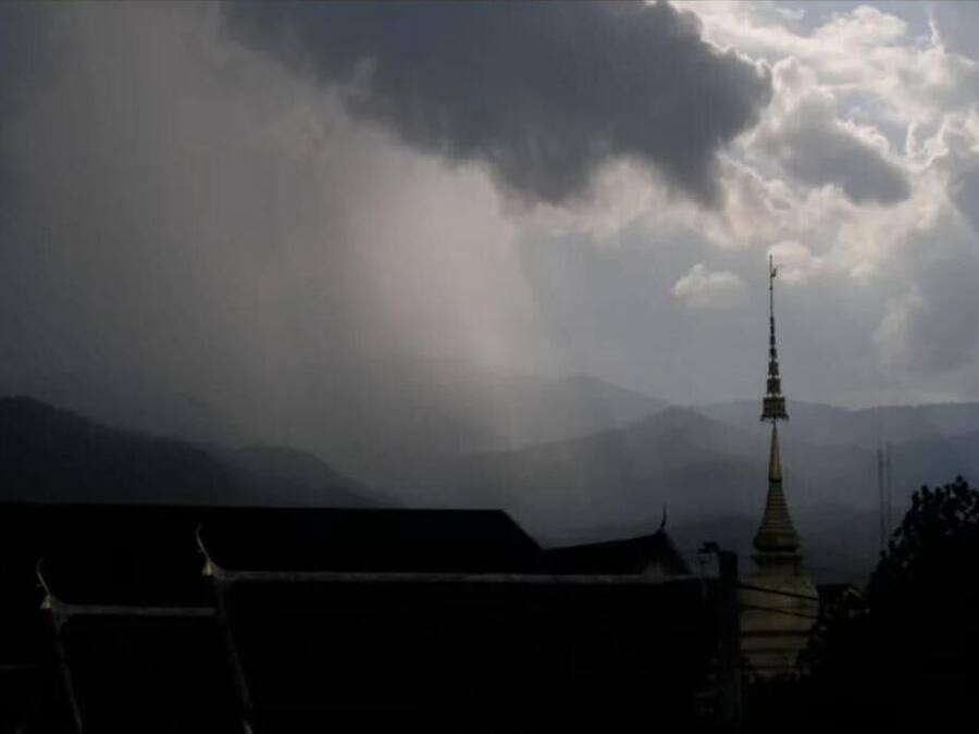 Um edifício tradicional com telhado pontiagudo e torre, com montanhas e céu nublado ao fundo.