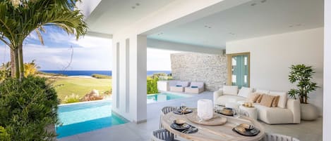 Ein moderner Essbereich im Freien mit Blick auf einen Pool, einer Steinwand und einem weißen Sofa.