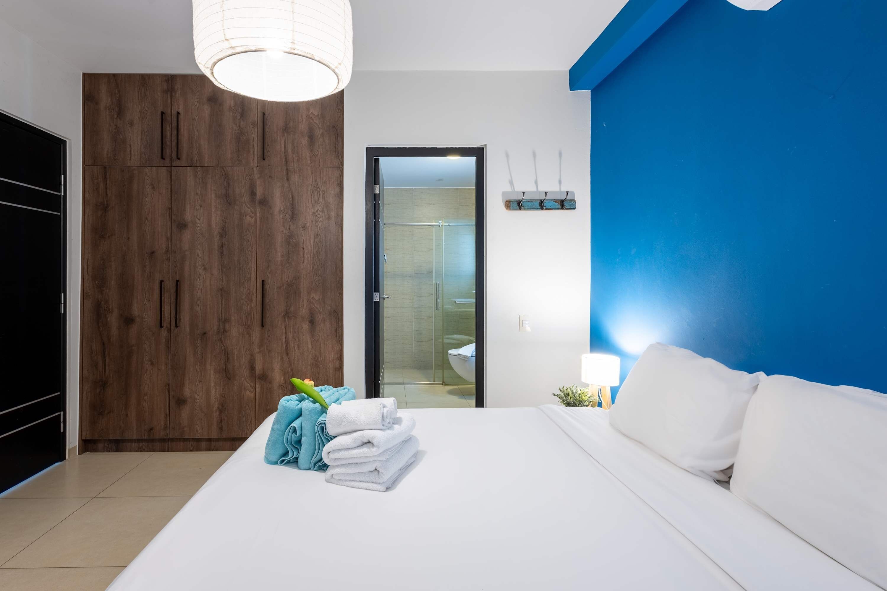 Un dormitorio con cama, armario, puerta de baño y mesita de noche con lámpara.