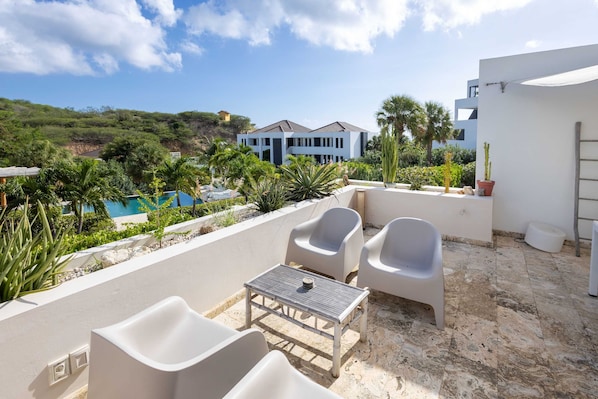 A terrace with outdoor seating, a pool, and a view of a modern building.