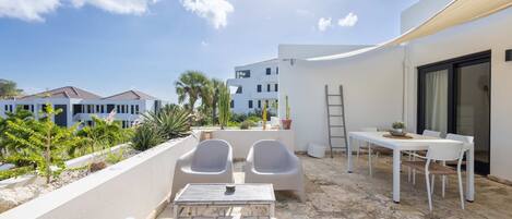 An outdoor patio with white furniture, a table, and chairs, surrounded by a white wall and plants.