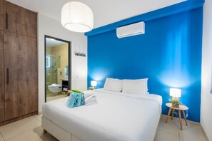 A hotel room with a large bed, a wooden wardrobe, a bathroom visible through an open door, and a blue accent wall.