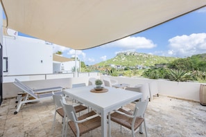 A patio with a table and chairs, a view of a hill, and a white building in the background.
