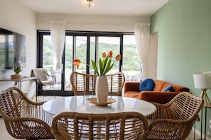 A dining area with wicker chairs, a round table, and a vase with flowers.