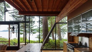 Una cocina moderna con ventanas amplias, techo de madera y vistas a árboles y agua.