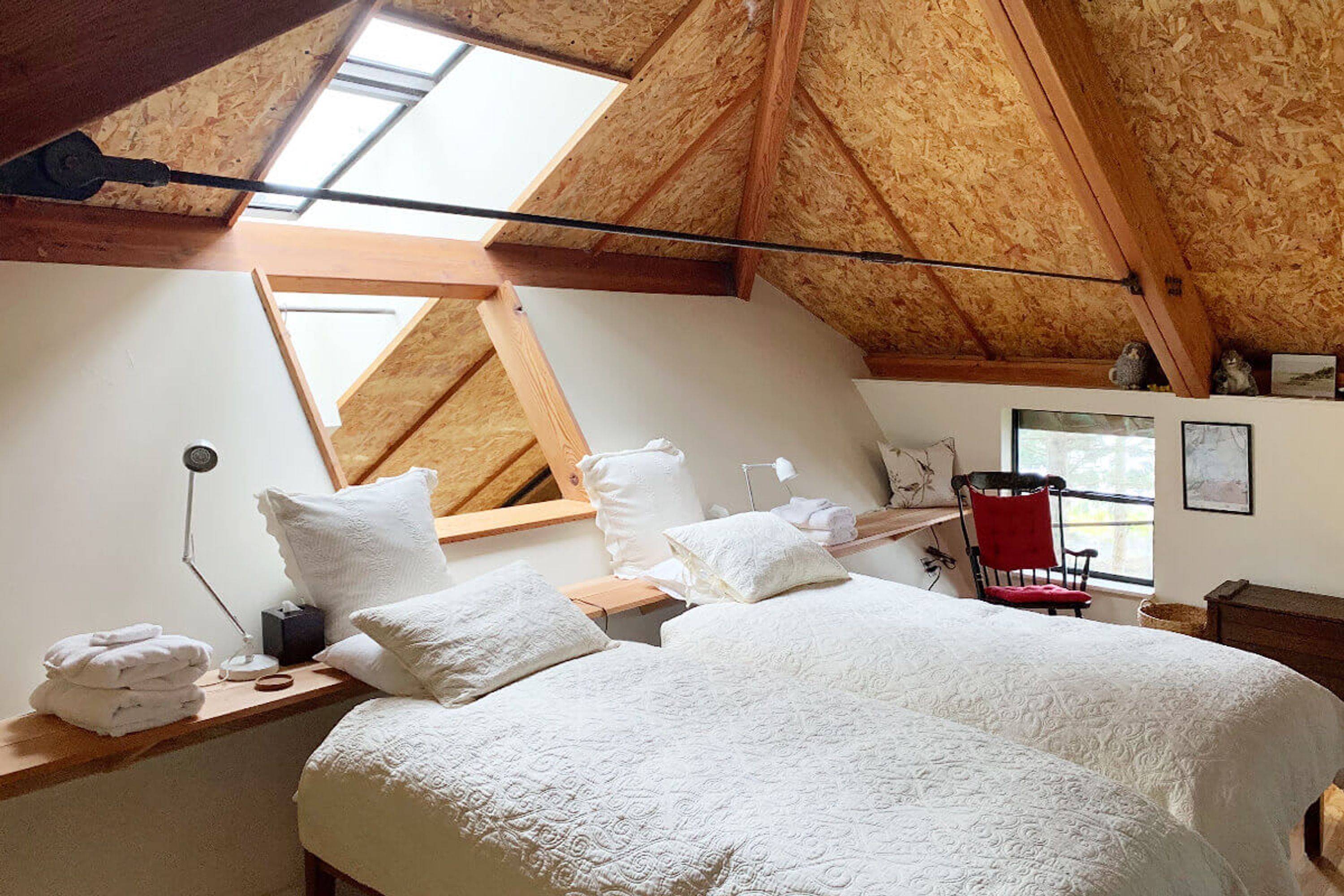 Ein Schlafzimmer mit schrägem Dach, einem Bett mit weißer Bettwäsche, einem Fenster und einem Spiegel.