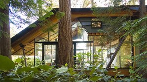 Una cabaña moderna con amplios ventanales, rodeada de un bosque denso.