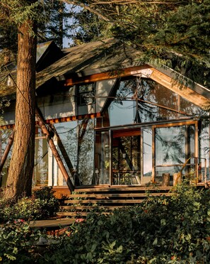 A modern cabin with large windows, wooden beams, and a rustic setting surrounded by trees. - Conner Glass Cabin by Boutique (La Conner)