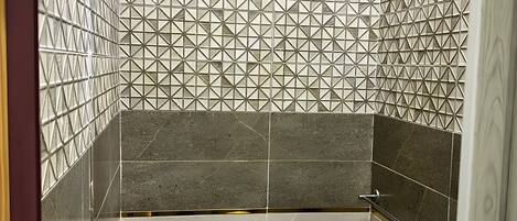 A bathroom with a toilet, bidet, and sink, featuring geometric patterned tiles and a shower head.