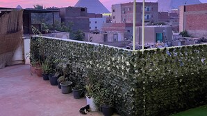 A rooftop garden with potted plants and a ladder, overlooking a cityscape with pyramids in the background. - Jana pyramids view inn (Giza)