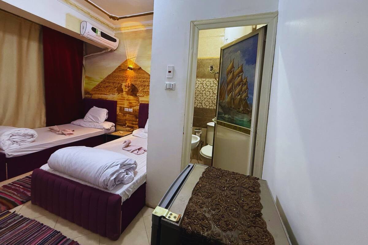 A hotel room with two beds, a bathroom with a painting, and a small table with a decorative item.
