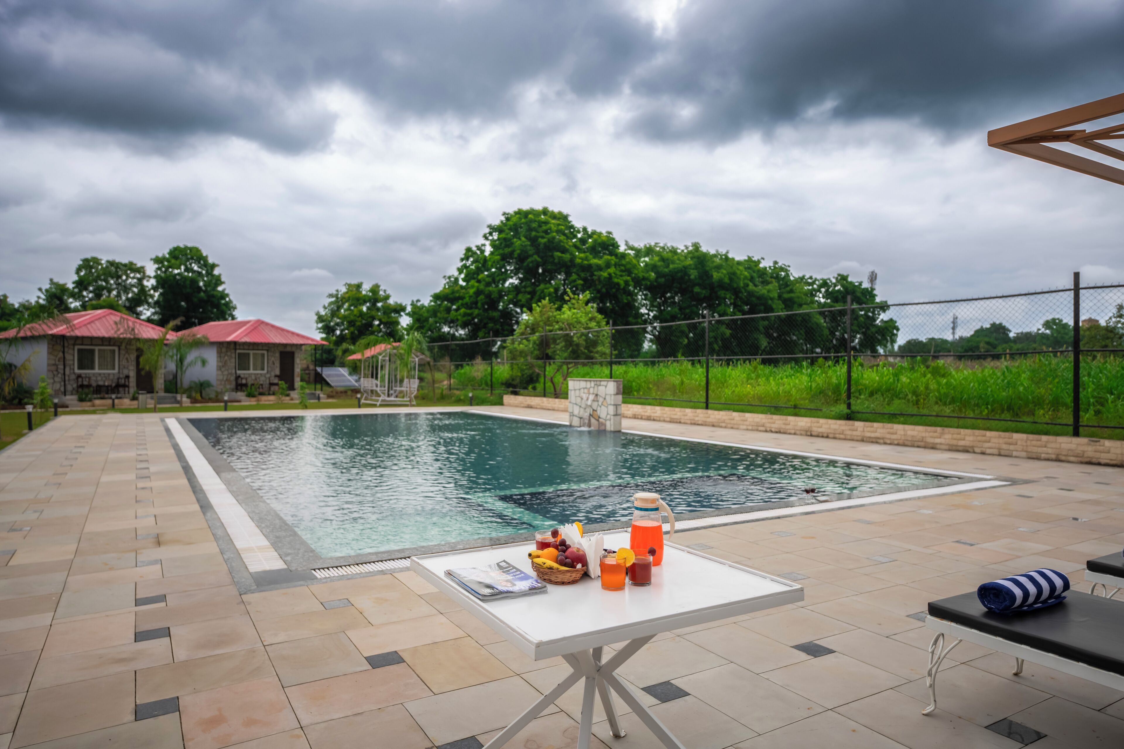 A swimming pool with a table and drinks, surrounded by a fence and greenery.