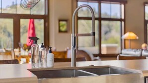A modern kitchen with a stainless steel sink, a hanging light fixture, and a window with a view of the outdoors.