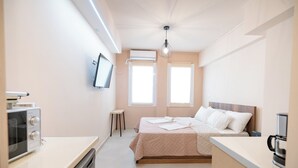 A modern hotel room with a kitchenette, a bed with a wooden headboard, two windows with blinds, and a ceiling light fixture. - Monastiraki metro st studio for 2 persons by MPS (Athina)