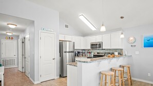 Une cuisine moderne avec des meubles blancs, des appareils en acier inoxydable, un comptoir en granit et des tabourets de bar en bois.