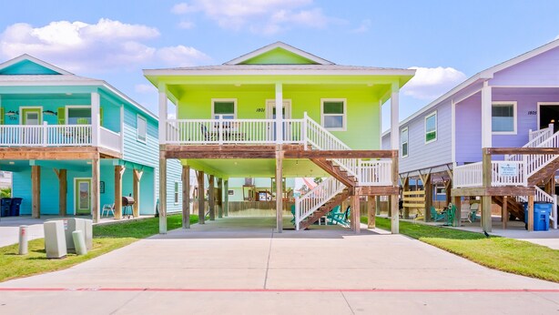 Un hôtel situé en bord de mer, avec un bâtiment principal de couleur verte, deux bâtiments latéraux et des passerelles en bois.