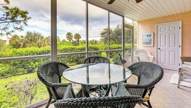 A covered patio with a glass table surrounded by wicker chairs, overlooking a lush garden. - 8 Mi to Beach w/ Pool Access: Englewood Condo! (Englewood)
