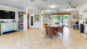 A spacious living room with a dining area, ceiling fans, a TV, and a bookshelf. - 8 Mi to Beach w/ Pool Access: Englewood Condo! (Englewood)
