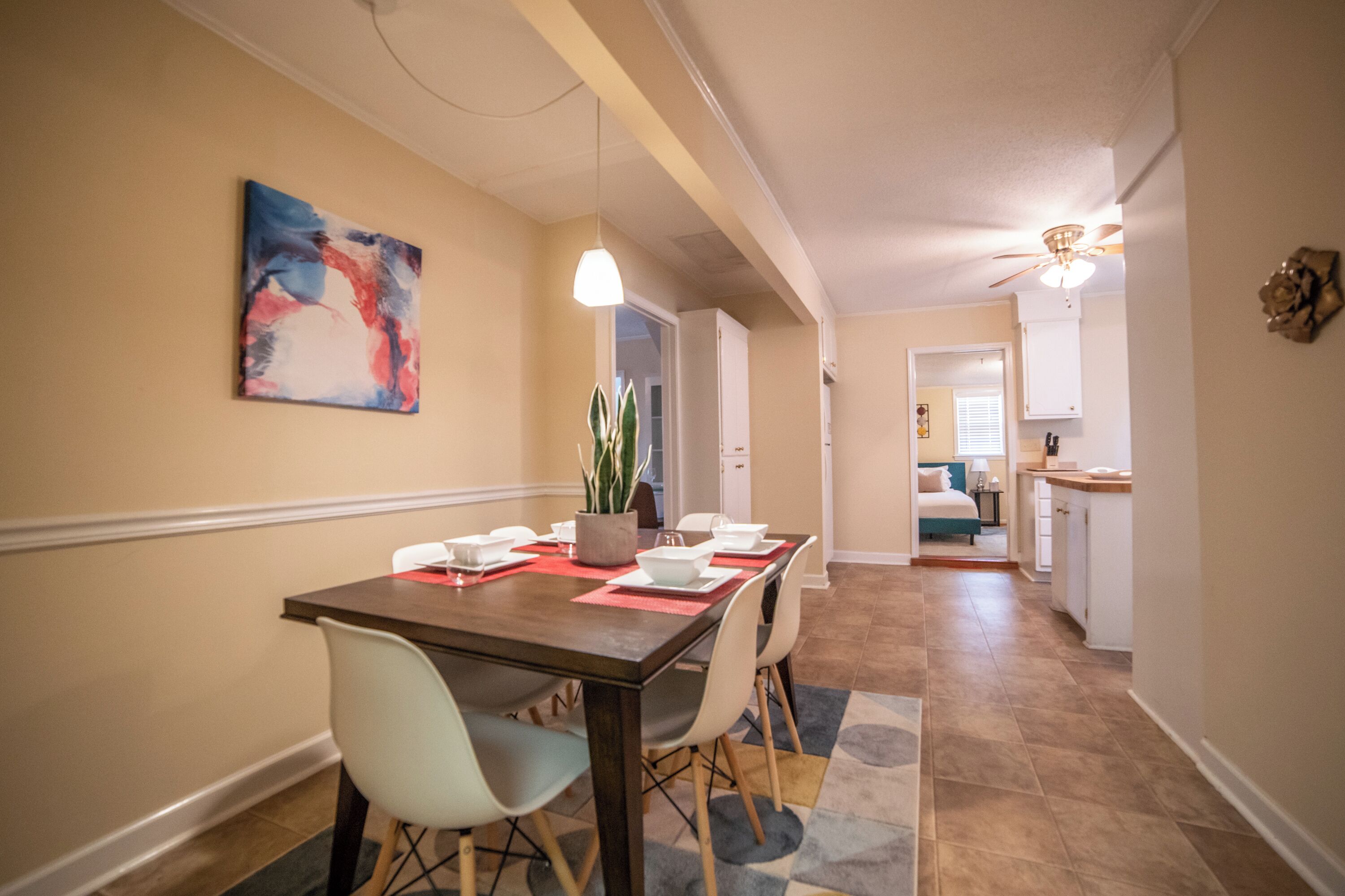 A dining area with a table set for four, chairs, a potted plant, and a colorful abstract painting on the wall.