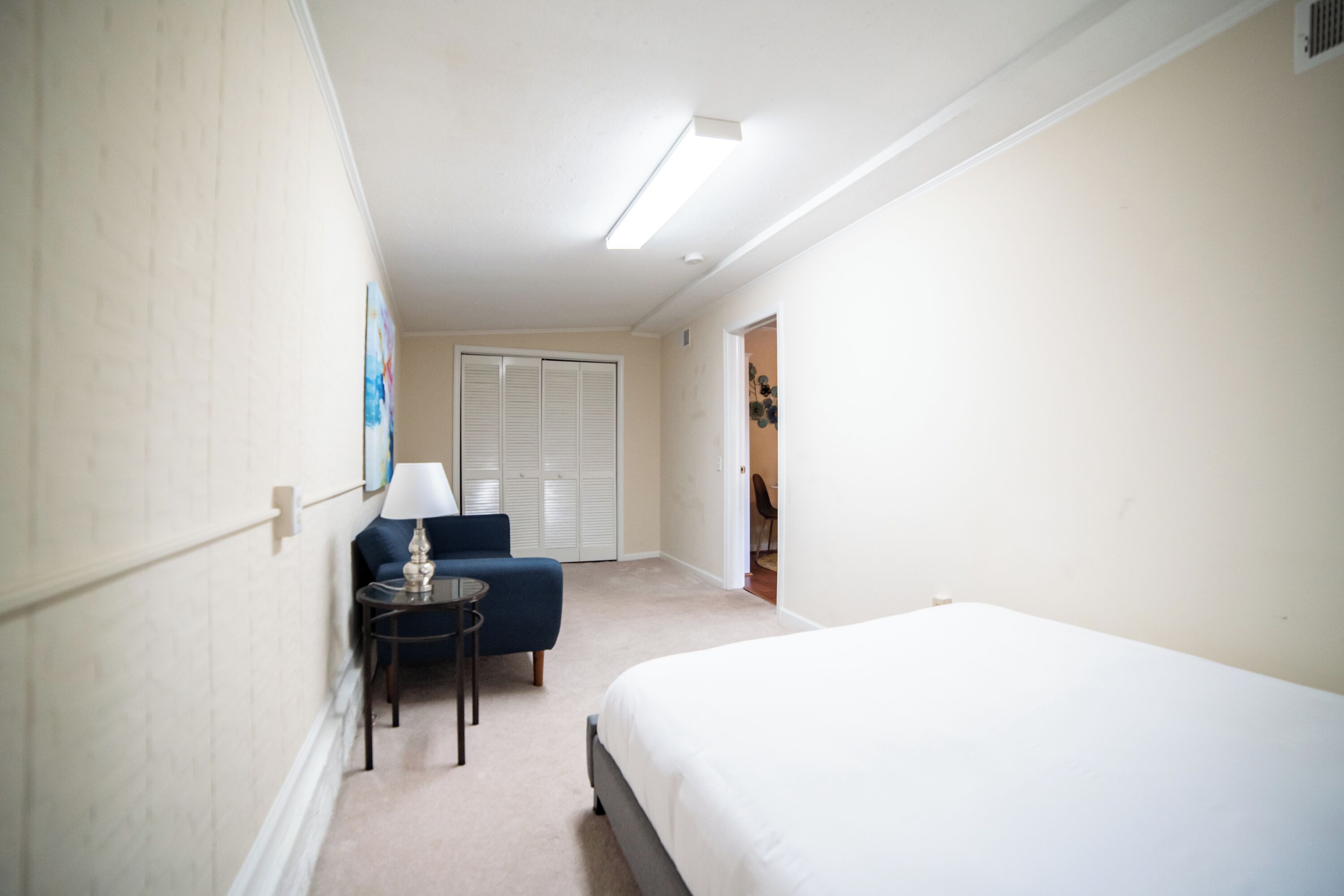 Una habitación de hotel con una cama, un escritorio con lámpara, una silla y un armario.