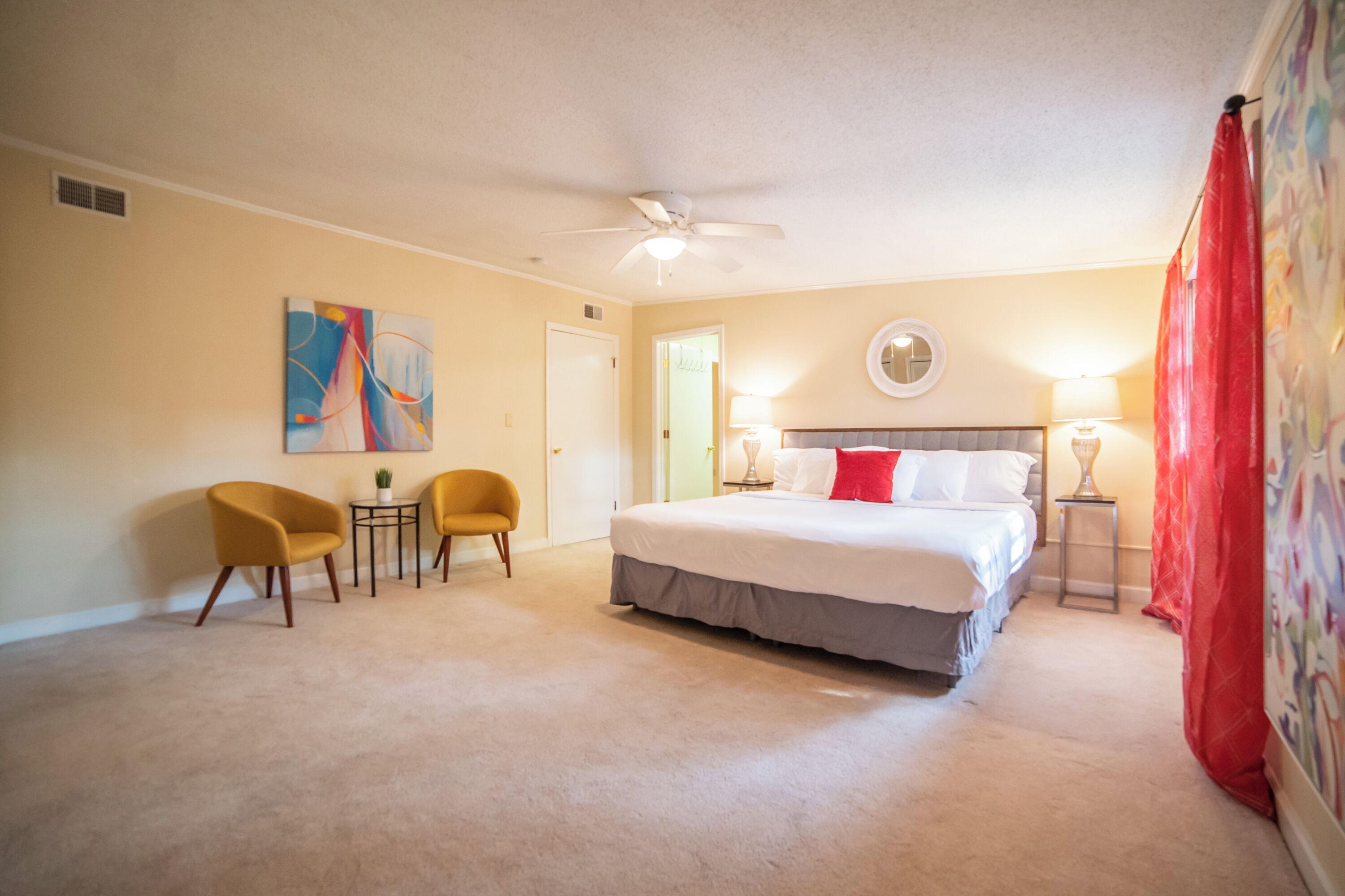 A hotel room with a large bed, two chairs, a ceiling fan, and a small table.