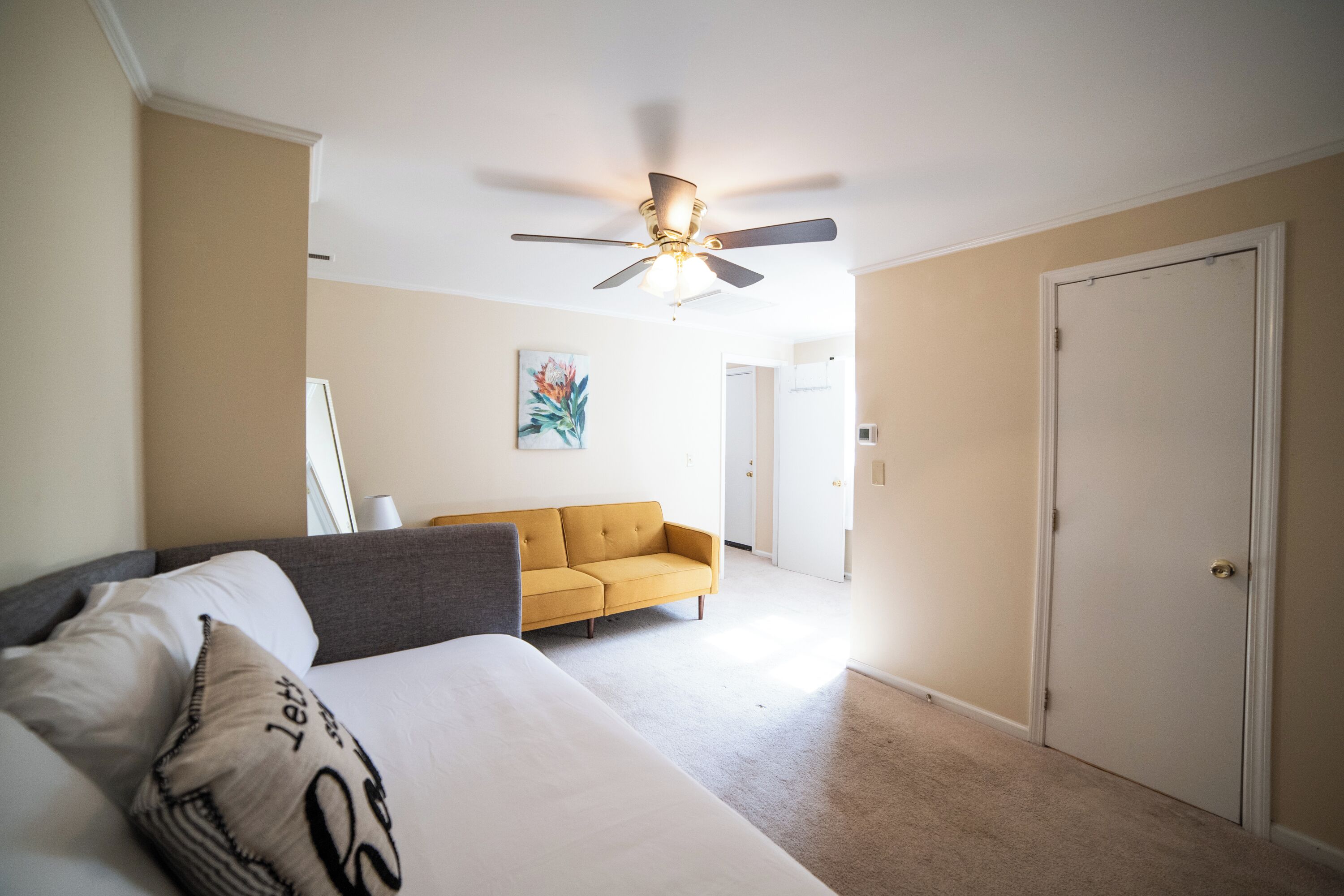 A bedroom with a bed, a sofa, a ceiling fan, and a door.