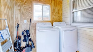 A laundry room with two white washing machines, a vacuum cleaner, and a broom. - Pet Friendly & Private 3BR Raised Home, Blocks to the Beach! (North Myrtle Beach)