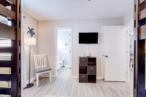 A hallway with a white door, a flat-screen TV mounted on the wall, a white chair, and a floor lamp.