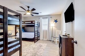 A bedroom with bunk beds, a ceiling fan, a desk with a lamp, a chair, and a television on the wall.
