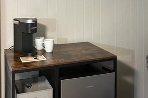 Una macchina da caffè compatta su un tavolo di legno, con due tazze bianche e un sottobicchiere.