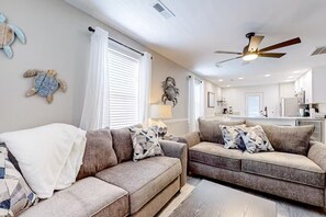 A living room with two sofas, a ceiling fan, and a kitchen in the background.