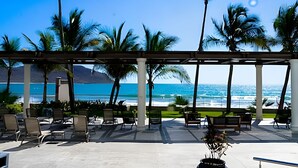A covered outdoor seating area with chairs and tables, overlooking a beach with palm trees and a clear blue sky. - Beach and luxury with ideal location (Mazatlán)