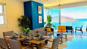 A dining area with a table set for four, a sofa, and a chair with a view of the sea. - Beach and luxury with ideal location (Mazatlán)
