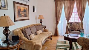 Una sala de estar con un sofá, dos lámparas, una silla, una mesa de vidrio y un cuadro en la pared.