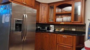 Una cocina con armarios de madera, un refrigerador de acero inoxidable, un microondas y una cafetera.
