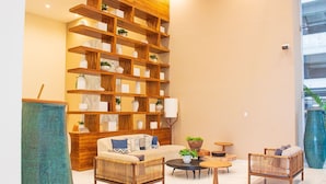 Ein Wohnzimmer mit einer großen Holzbücherwand, einer Couch, zwei Sesseln, einem Couchtisch und einer Stehlampe.