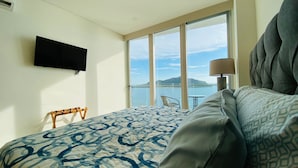 Ein Hotelzimmer mit einem großen Bett, einem flachbildfernseher an der Wand, einem Balkon mit Meerblick und einem Tisch mit Stühlen.