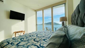 Une chambre d’hôtel dotée d’un grand lit, d’un téléviseur à écran plat fixé au mur, d’un balcon avec vue sur la mer et d’une table avec des chaises.