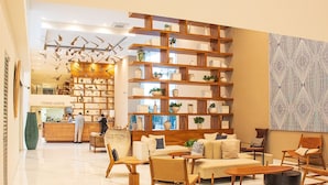 Ein modernes Interieur mit einer zentralen Holzbibliothek, einer Sitzecke mit Sofas und Sesseln sowie einer Wand mit Musterdesign.