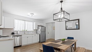 Una cocina moderna con armarios blancos, un refrigerador de acero inoxidable y una mesa de comedor de madera con sillas azules.
