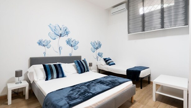 Une chambre à coucher avec un grand lit, deux tables de chevet, une commode, un bureau et une fenêtre avec des stores.