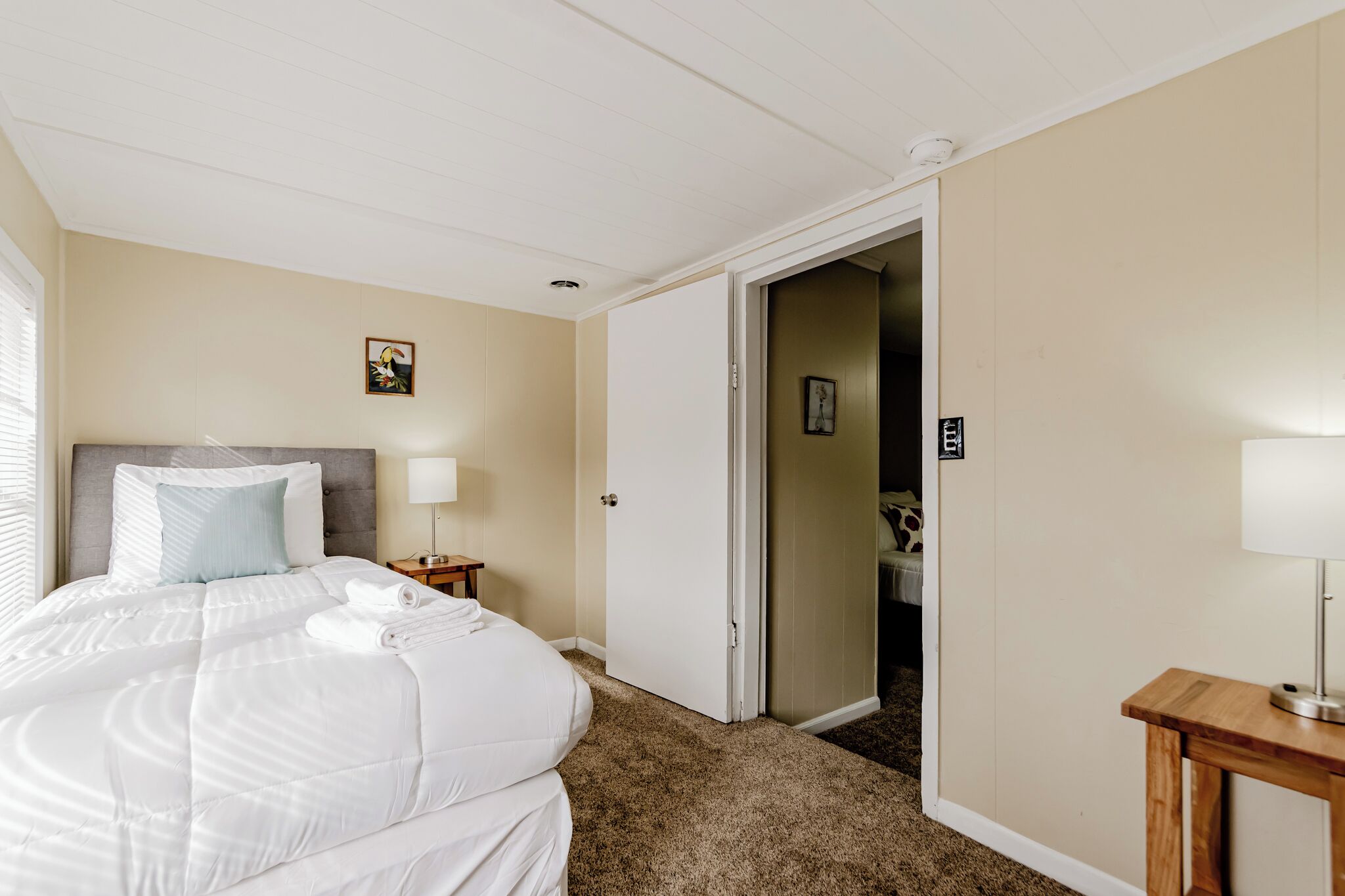 Une chambre d’hôtel comprenant un lit, une table de chevet, une porte donnant accès à une salle de bain et une petite table avec une lampe.
