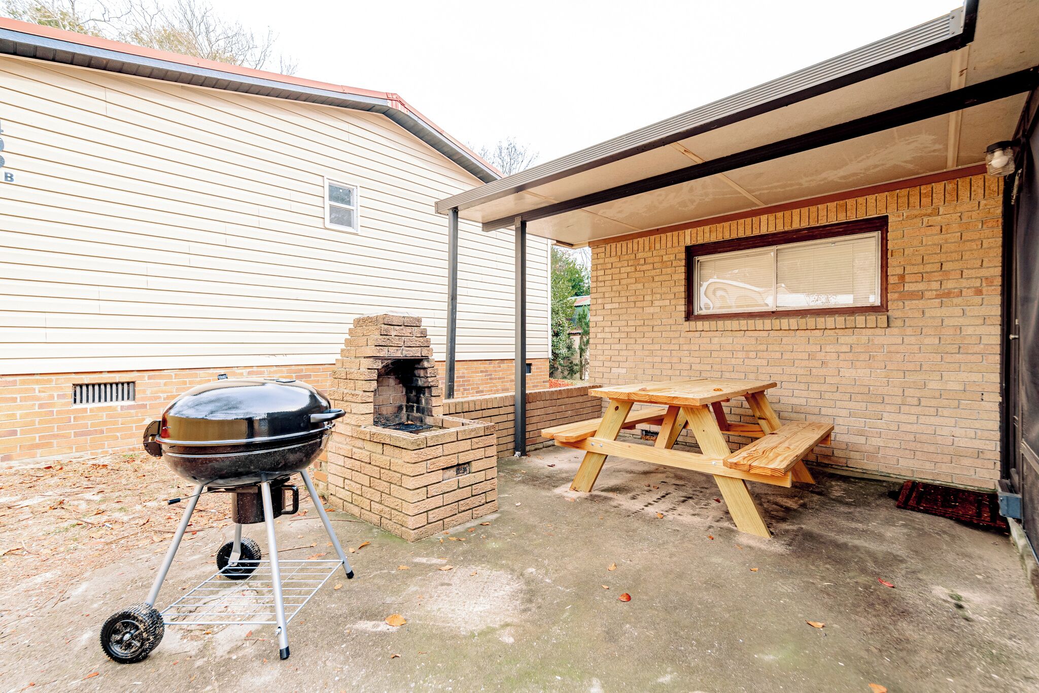 Een achtertuin met een bakstenen barbecue, een houten picknicktafel en een bakoven.